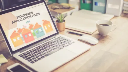 A laptop displaying a mortgage application form with colorful house icons on a wooden desk setup.