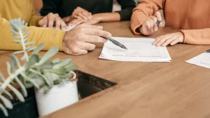 Close-up of hands signing documents at a business meeting with a plant in the foreground.