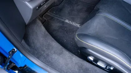 Black car floor mat labeled Emir with leather and suede seat featuring yellow stitching inside blue vehicle