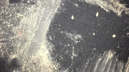 Fine light-colored powder scattered and smeared on a dark textured surface with streaks and small clumps