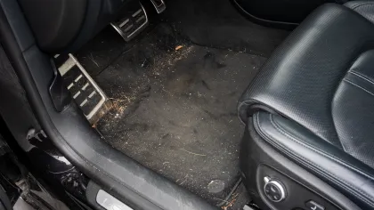 Dirty black car floor mat with debris and stains near the driver's seat and pedals
