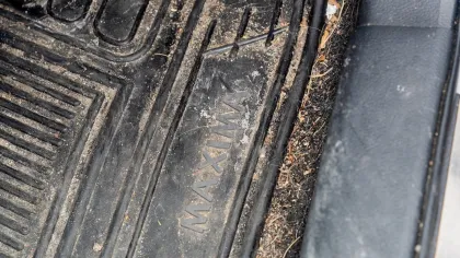 Dirty black rubber car floor mat with dirt and debris, labeled MAXIMA, inside vehicle door frame.