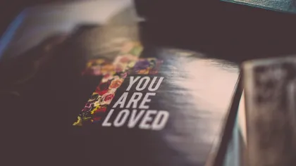 Close-up of a book cover with a floral cross and the message You Are Loved in soft lighting.
