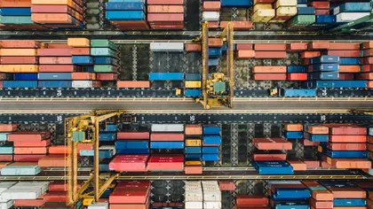 Aerial view of colorful shipping containers and yellow cranes at a busy logistics port yard.