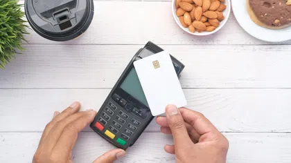 Person using contactless payment card on a terminal with coffee, almonds, and cookies on white table
