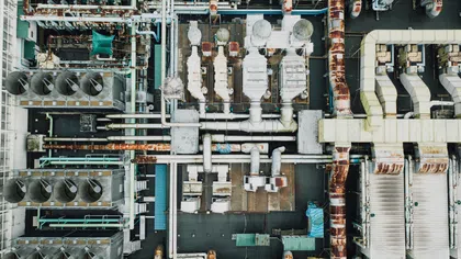 Aerial view of an industrial facility with extensive rusted pipelines, cooling ducts, and mechanical equipment.