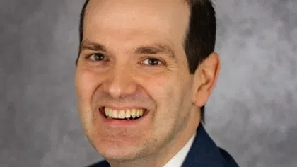 Smiling man in business suit with pink striped tie against a gray textured background.