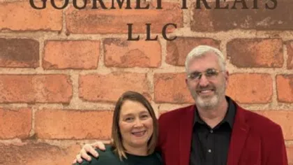 Two smiling people stand in front of a brick wall with Winters Gourmet Treats LLC logo featuring a chocolate piece.