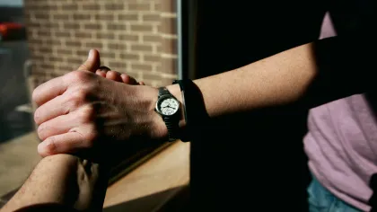 Close-up of two hands clasped together near a sunlit window with one person wearing a watch.