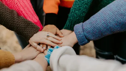 Group of people wearing colorful sweaters stacking hands in a gesture of unity and teamwork.
