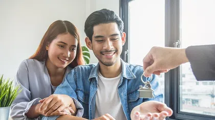 Happy couple receiving house keys from agent in bright modern office with documents and laptop on table
