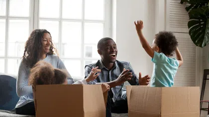 Happy family playing and laughing with cardboard boxes in a bright living room filled with natural light