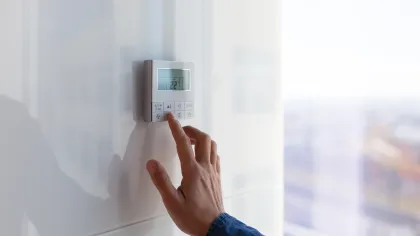 Hand adjusting a digital thermostat on a white wall in a modern indoor environment