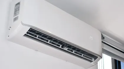 Wall-mounted white air conditioner unit set to 25 degrees Celsius installed near a window.