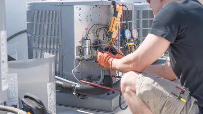 Technician repairing and testing outdoor air conditioning unit with tools and gauges on a sunny day