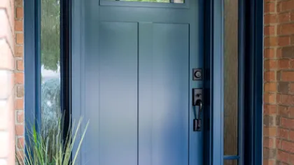 Modern blue front door with glass panels, black handle, brick entrance, and decorative rug with potted plant.