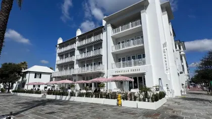 Modern white building with balconies and outdoor dining area under pink umbrellas on a sunny day