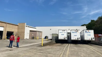 Loading dock area with three Walmart delivery trucks and two workers wearing red shirts under clear blue sky.