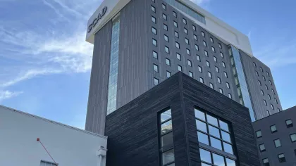 View of SCAD's tall modern building and Alexander Hall under a blue sky with wispy clouds.