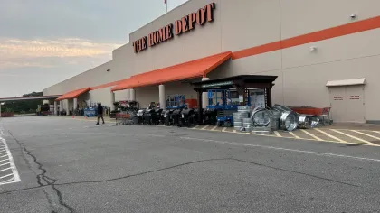 Wide exterior view of The Home Depot with outdoor grills, metal ducts, and shopping carts under overcast sky.