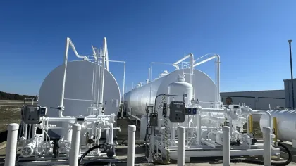 Large white industrial storage tanks with connected piping and machinery under clear blue sky outdoors.