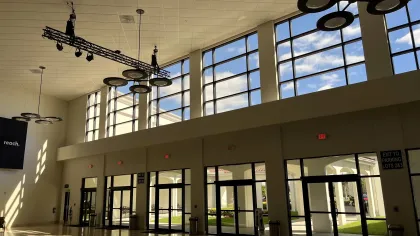Bright modern lobby with large windows, glass doors, and circular ceiling light fixtures casting shadows.