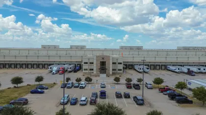 Warehouse distribution center with parked trucks and cars under a partly cloudy blue sky.