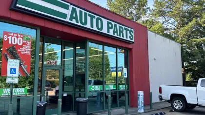 Exterior of an auto parts store with green signage and a white pickup truck parked nearby on a sunny day.