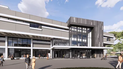 Modern Humanities building with large glass entrance, people walking and chatting outside on a sunny day.