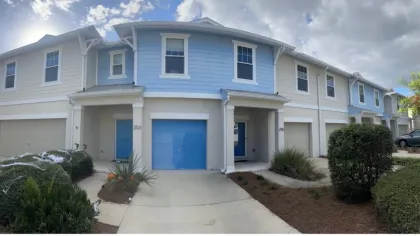 Two similar townhouses with blue and beige exteriors, featuring garages, front doors, and landscaping under different lighting.