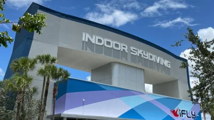 Exterior of iFLY indoor skydiving facility with bold sign and tropical palm trees under a bright blue sky.