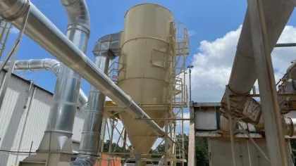 Industrial silo with attached metal pipes and ducts under a blue sky with some clouds during daytime.