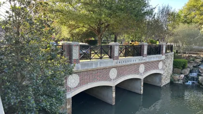 Brick and stone bridge over calm water with trees and greenery in University Park on a sunny day