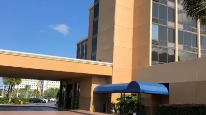 Exterior of a beige multi-story building with glass windows, blue canopy entrance, and clear blue sky above.