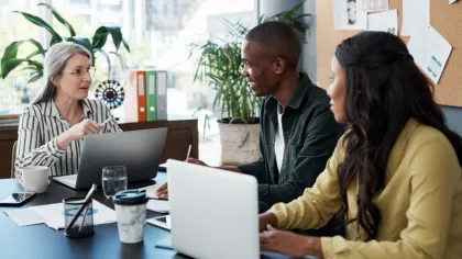 a group of people sitting around a table with laptops