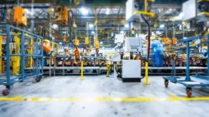 Modern factory floor with workers, robotic arms, and machinery assembling products under bright lighting.