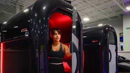 Woman exiting a black infrared sauna pod with red interior lighting in a modern wellness facility.