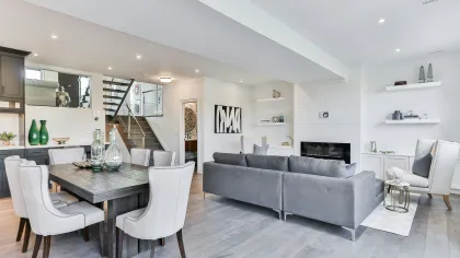 Modern open-concept living and dining room with gray sofa, beige chairs, wooden table, and minimalist decor.