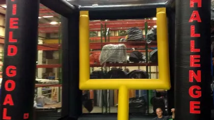 Inflatable football field goal challenge game with a man holding a football inside the setup in a warehouse.
