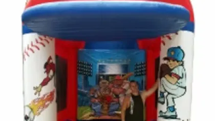 Man standing inside a colorful baseball-themed inflatable bounce house with painted players and baseballs.