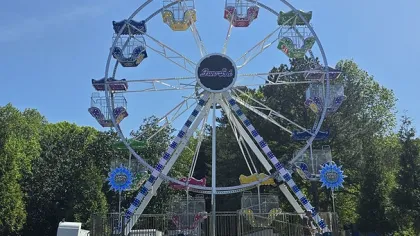 Colorful Ferris wheel with multi-colored seats set up outdoors on a sunny day with trees and empty parking lot