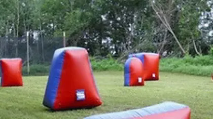 Inflatable paintball field bunkers in red and blue set up on a grassy outdoor area with trees in the background
