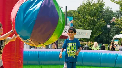 Children playing with a large colorful inflatable ball in a vibrant outdoor play area on a sunny day