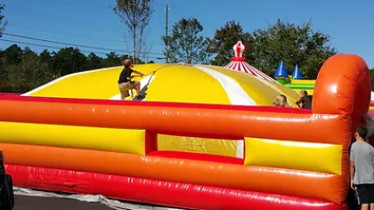 Children playing on a large yellow and white inflatable bounce house outdoors on a sunny day.