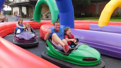 Children and adults enjoying bumper cars on a colorful inflatable track at an outdoor event.