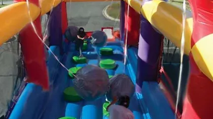 People playing on an inflatable obstacle course with large swinging balls and green platforms outdoors.
