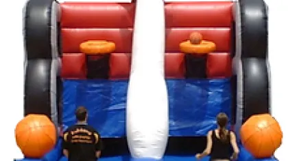 Inflatable basketball game with two people aiming to shoot basketballs into hoops on a vibrant red and blue setup.