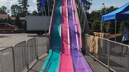 Colorful three-lane outdoor fun slide with teal, pink, and purple lanes at a sunny carnival setting.