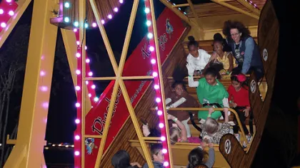 Children enjoy a brightly lit swinging pirate ship ride at night in an amusement park or fair.