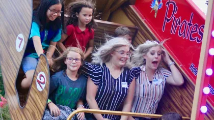 Group of children and adults enjoying a pirate ship amusement park ride with expressions of excitement and joy.